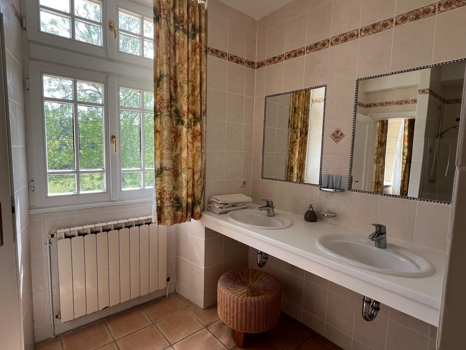 Un baño con dos lavamanos, un espejo grande, un radiador y una ventana con cortinas.