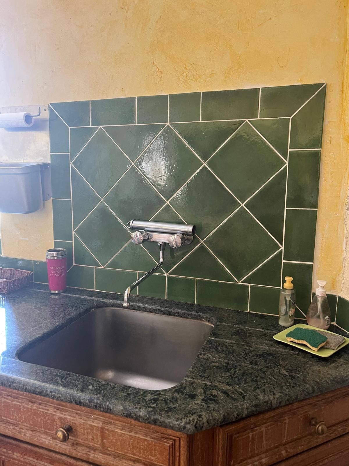Cocina con lavamanos, salpicadero de azulejos verdes y encimera de granito.
