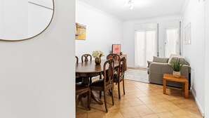 A dining area with a wooden table and chairs, a sofa, and a small side table with a plant.