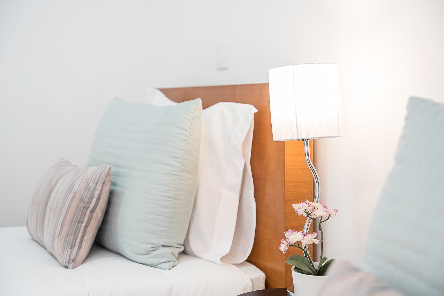 Une chambre d’hôtel avec un lit, des oreillers, une table de chevet avec une lampe et une orchidée en pot.