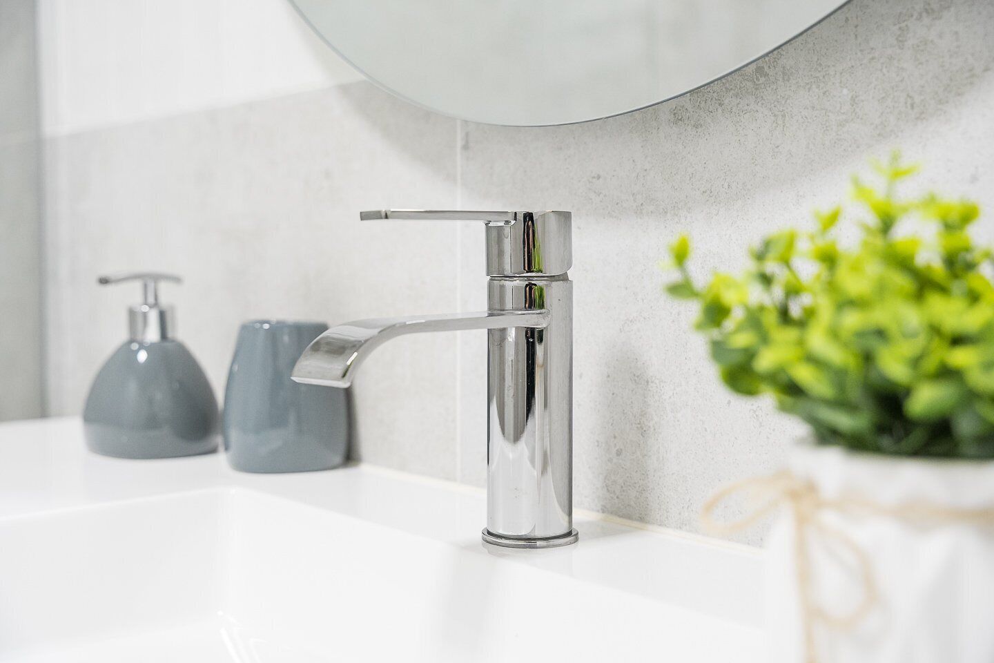 A modern bathroom with a chrome faucet, a mirror, and a small plant.
