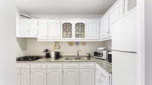 A kitchen with white cabinets, a granite countertop, a stove, a sink, and two ovens.