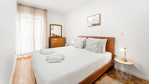 A bedroom with a bed, a dresser, a mirror, a bedside table with a lamp, and a picture on the wall.