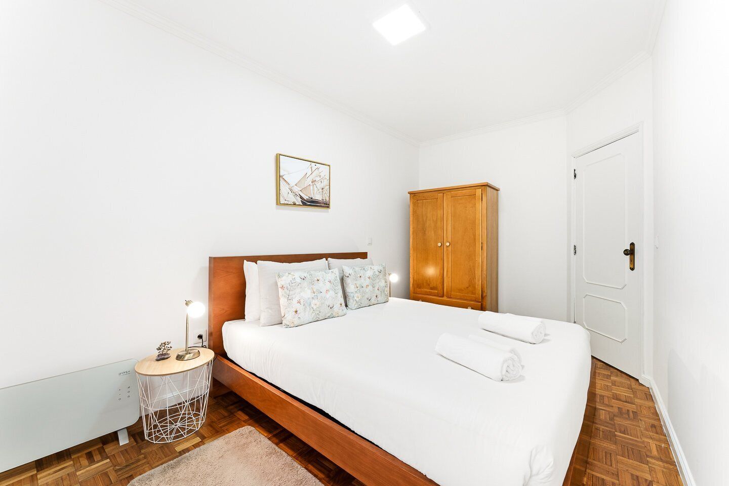 Ein Schlafzimmer mit einem hölzernen Bett, weißen Wänden, einem Holzschrank und einem kleinen Nachttisch mit einer Lampe.