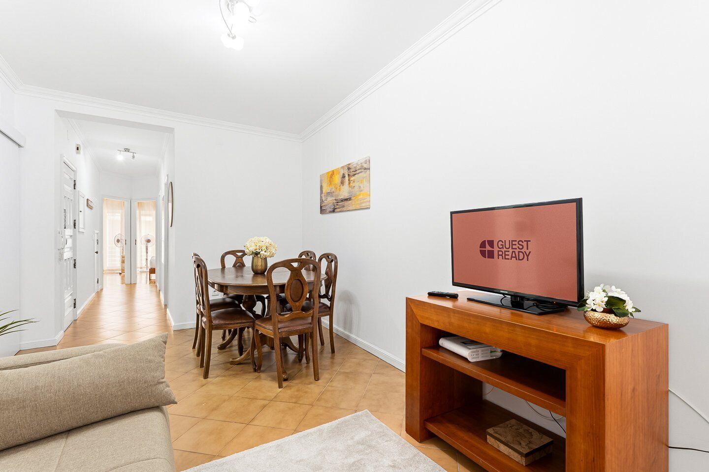 Een hotelkamer met een zithoek, een televisie op een houten standaard en een gang naar een andere kamer.