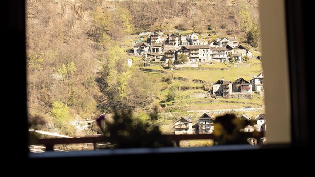 A view through a window with heart-shaped decorations, a rural landscape with houses, and a mountain in the background.