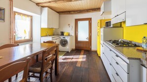 A kitchen with wooden cabinets, a washing machine, a dining table with chairs, and a view through a door.