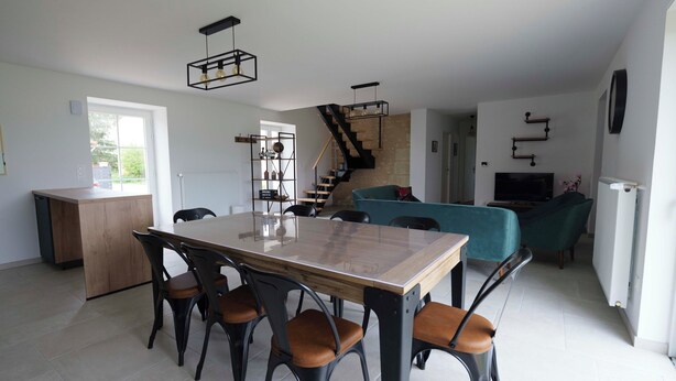 A modern kitchen with a dining table and chairs, a staircase, and a living area with a sofa.