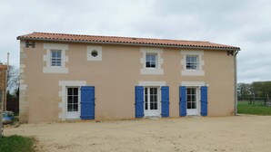 A two-story building with a beige facade, white window frames, and blue shutters.