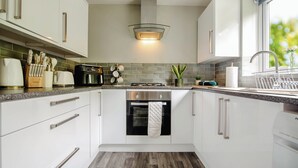 Una cucina moderna con mobili bianchi, un forno in acciaio inox, una cappa aspirante integrata e una finestra con vista.