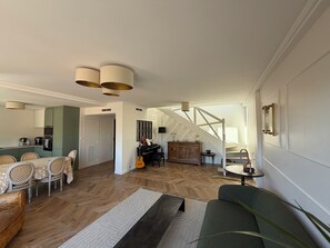 A spacious living area with a dining set, a sofa, a staircase, and a kitchen in the background. - Large 105m² Apt with Terrace & Parking (Toulouse)