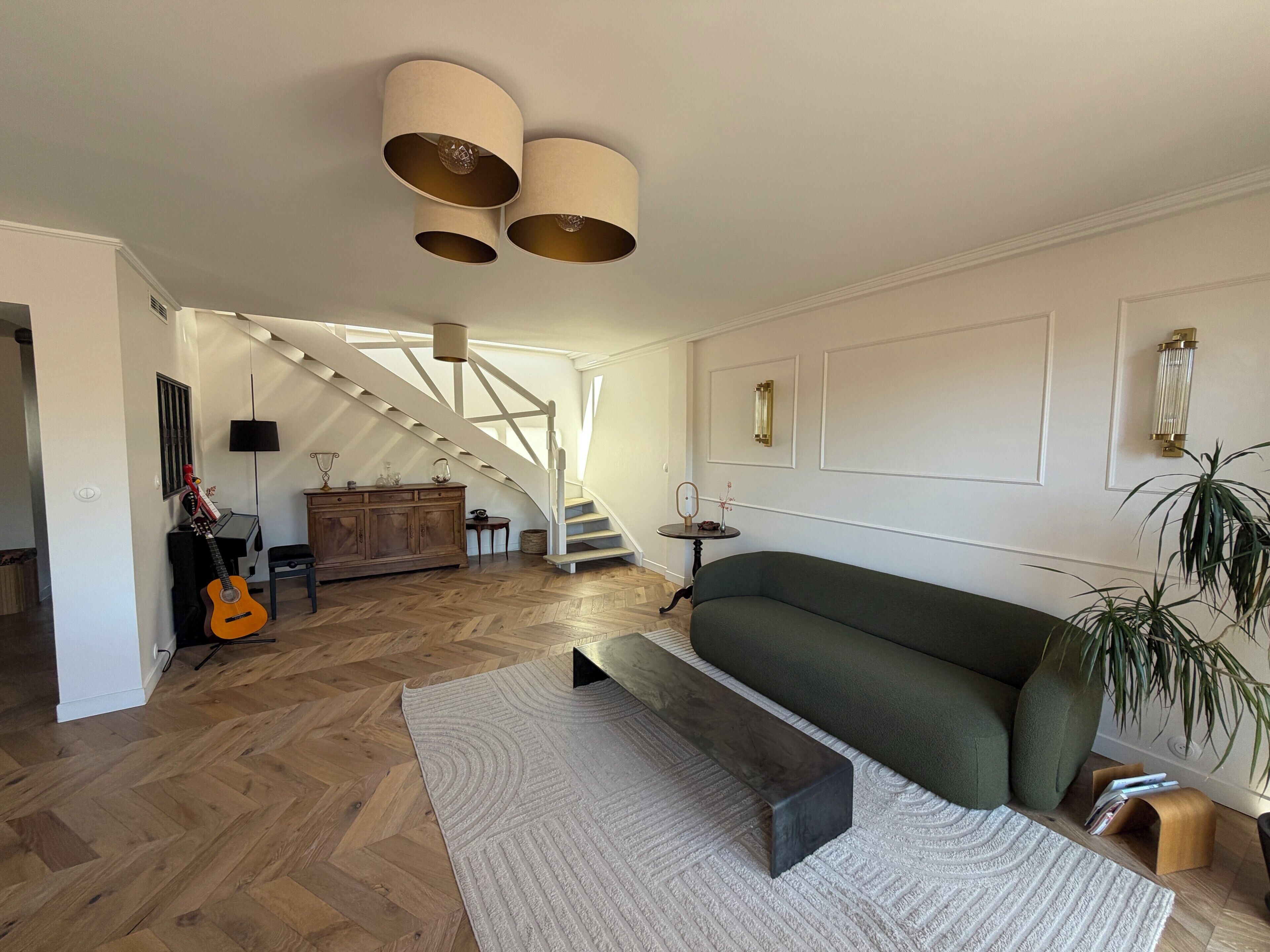 Een ruime woonkamer met een trap, een groene bank, een piano en een gitaar.