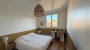Ein Schlafzimmer mit einem Bett, einem Schreibtisch, einem Sessel, einer Lampe und einem Fenster mit Blick auf die Stadt.