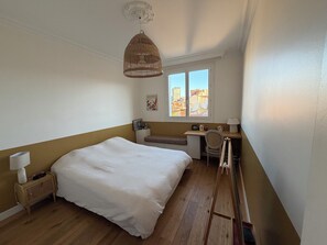 A bedroom with a bed, a desk, a chair, a lamp, and a window with a city view. - Large 105m² Apt with Terrace & Parking (Toulouse)