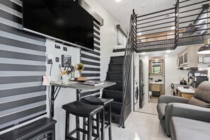 Un espacio habitable compacto con kitchenette, comedor, sofá y escalera.