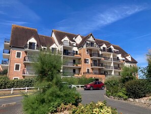 A multi-story residential building with balconies, a red car parked in front, and a clear blue sky. - Renovated and Bright Apartment - Direct Sea Access (Cabourg)