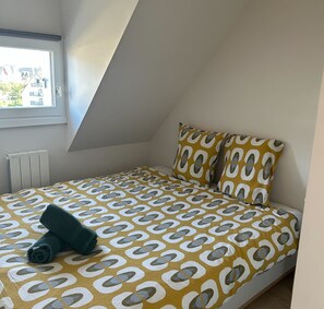 A small, triangular attic bedroom with a bed, pillows, and a rolled-up towel. - Renovated and Bright Apartment - Direct Sea Access (Cabourg)