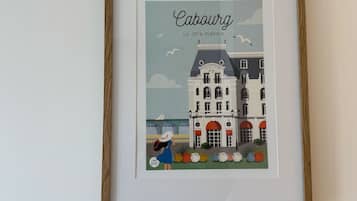 Eine gerahmte Illustration eines Gebäudes mit der Aufschrift 'Cabourg - La Côte Fleurie', einem großzügigen Hotelschild, einem Segelboot und einer Person mit Koffer.