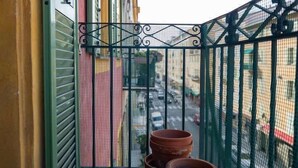Ein Balkon mit grüner Metallreling, einer geschlossenen grünen Tür und drei Terrakotta-Töpfen.