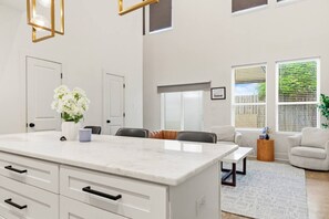 Una cocina moderna con una isla de mármol, armarios blancos y un comedor con mesa y sillas.