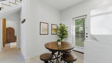 A dining area with a round table and stools, a potted plant, framed pictures on the wall, and a white appliance.