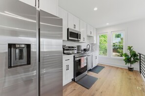 A modern kitchen with stainless steel appliances, white cabinetry, and a large window offering a view of greenery. - Private 2BR Brand New House w/Parking (Atlanta)
