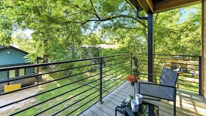 Une terrasse extérieure couverte, dotée d’une rambarde, d’une table avec des chaises et offrant une vue sur une serre et des arbres.