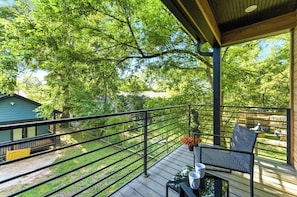 A covered outdoor deck with a railing, a table with chairs, and a view of a green house and trees. - Private 2BR Brand New House w/Parking (Atlanta)