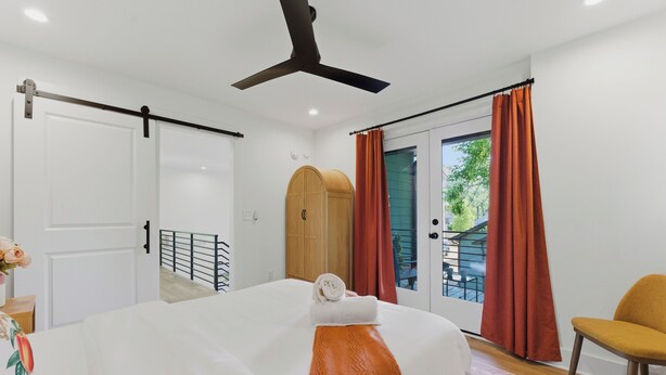 Une chambre d’hôtel avec un lit, un ventilateur de plafond, une porte coulissante donnant sur un balcon et une chaise.