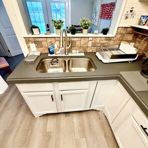 A kitchen with a stainless steel sink, white cabinets, and a stone backsplash.