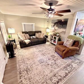 A living room with a ceiling fan, a sofa, a chair, a coffee table, and a rug. - The 1918 Magnolia Cottage (Milton)