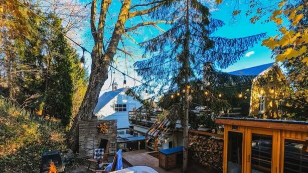 A hot tub in a backyard with a stone wall, wooden deck, and a view of a house.