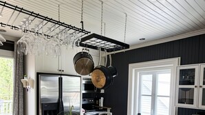 A modern kitchen with a wooden island, black chairs, stainless steel appliances, and a hanging pot rack.