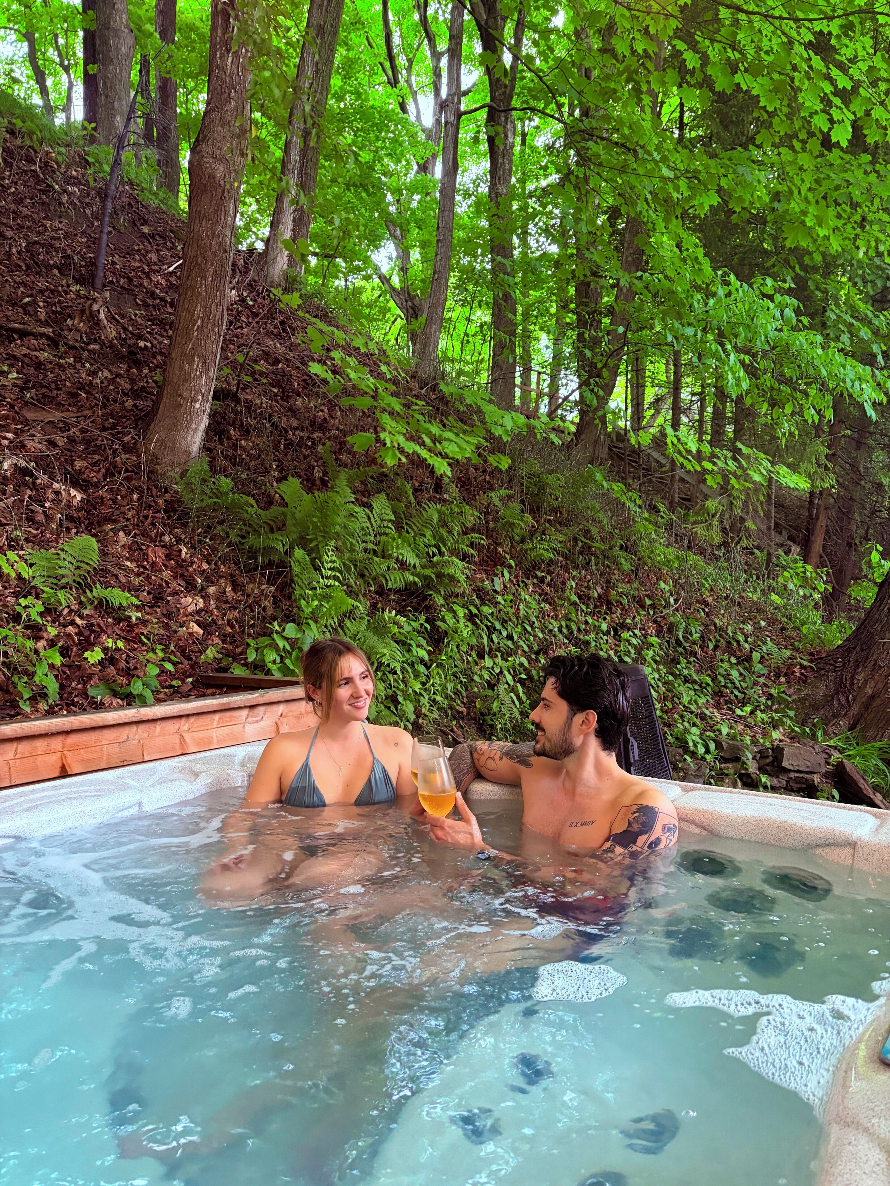 A couple in a hot tub surrounded by lush greenery.