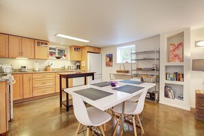 A modern kitchen with wooden cabinets, a white dining table with chairs, and a bookshelf with books. - Lovely 2-bedroom apartment in Seattle in vibrant Wallingford Neighborhood (Seattle)