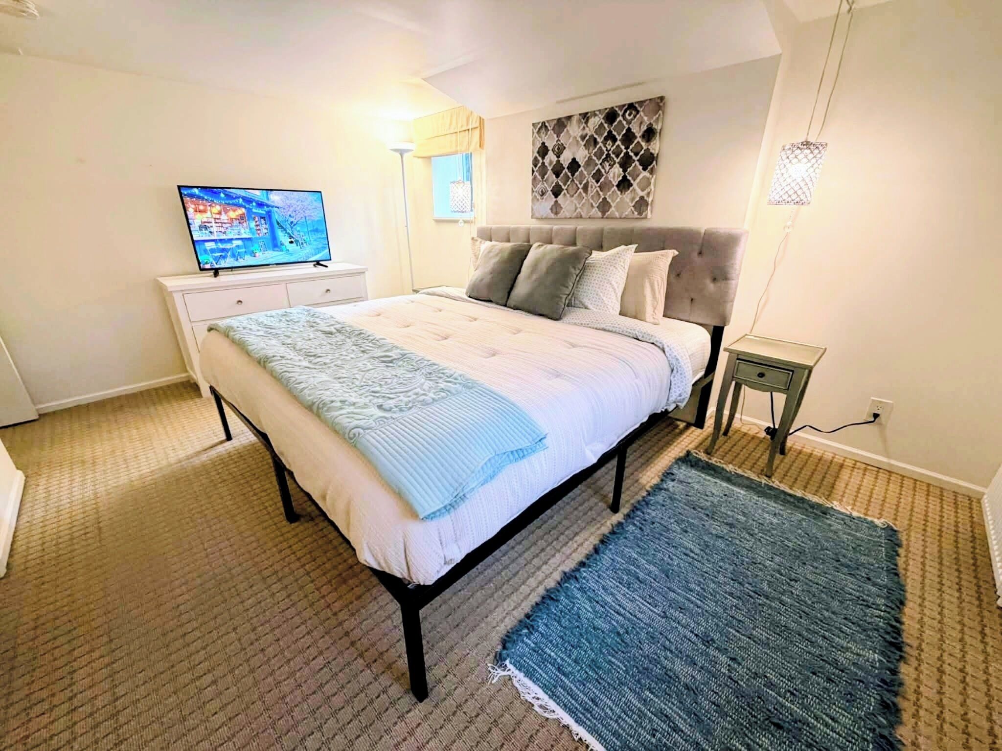 A bedroom with a bed, a TV, a bedside table, a lamp, and a patterned wall.