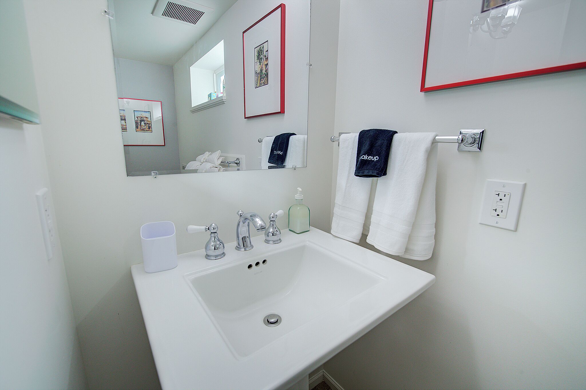 Un baño con un lavamanos blanco, dos llaves, un espejo y un cuadro en la pared.