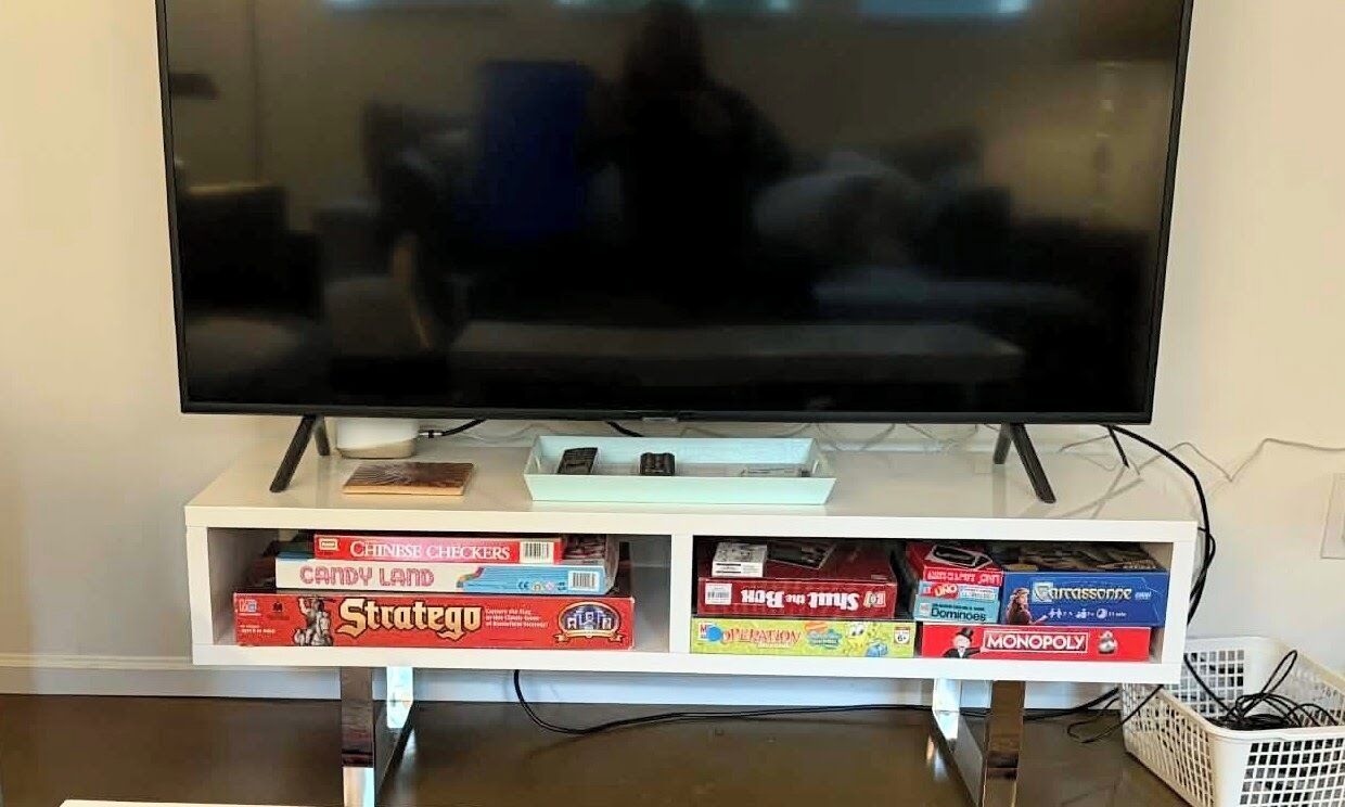 A television on a stand with a shelf below it holding board games.