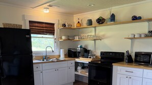Une cuisine avec des meubles blancs, un réfrigérateur noir, un plancher en bois et une fenêtre avec des stores.