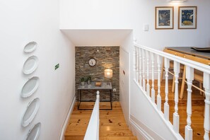 A staircase with a white railing, a wooden floor, a wall with a clock, a table with a lamp, and framed pictures on the wall. - Oporto Tiles Mezzanine by Hopstays | Marquês (Porto)