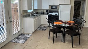 Cocina compacta con armarios blancos, microondas, estufa y una mesa de comedor con sillas.