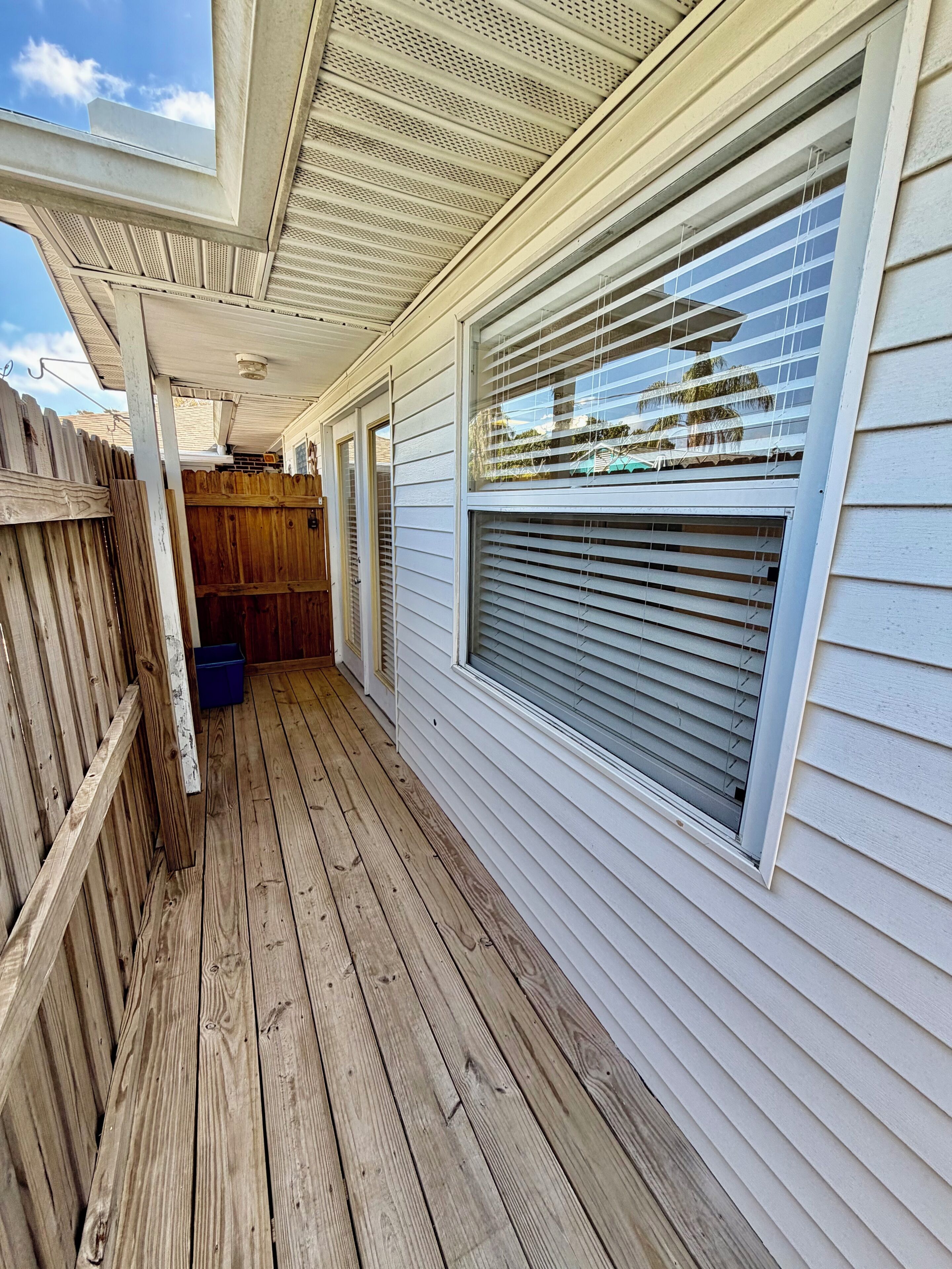 A covered wooden deck with a window and a wooden fence.