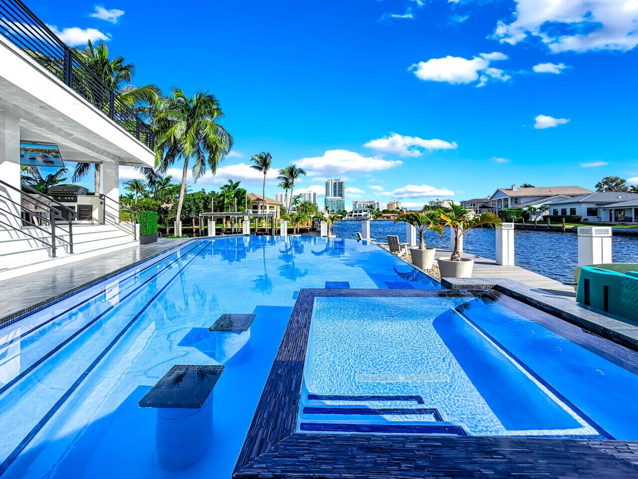 A swimming pool with a clear view of the water, surrounded by palm trees and buildings.