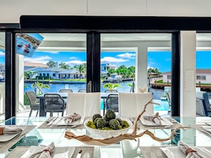 Ein Essbereich mit Blick auf einen Yachthafen und Gebäude, ein Glastisch mit dekorativem Mittelstück und ein modernes Interieur.
