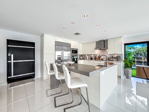 Una cocina moderna con una isla central, taburetes de bar, electrodomésticos de acero inoxidable y un amplio ventanal con vistas a zonas verdes.