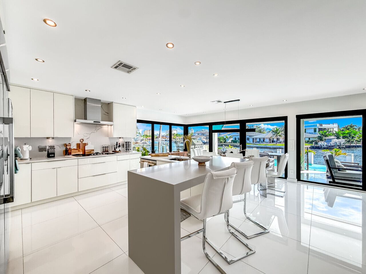 Una cocina moderna con una isla central, muebles blancos y vistas a un paisaje urbano a través de amplios ventanales.