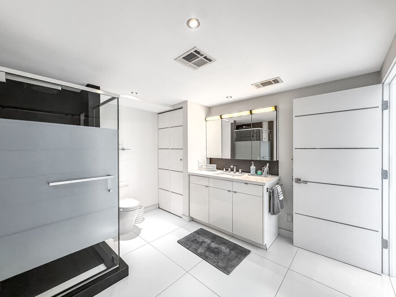 A modern bathroom with a glass shower enclosure, a large mirror, and a walk-in closet.