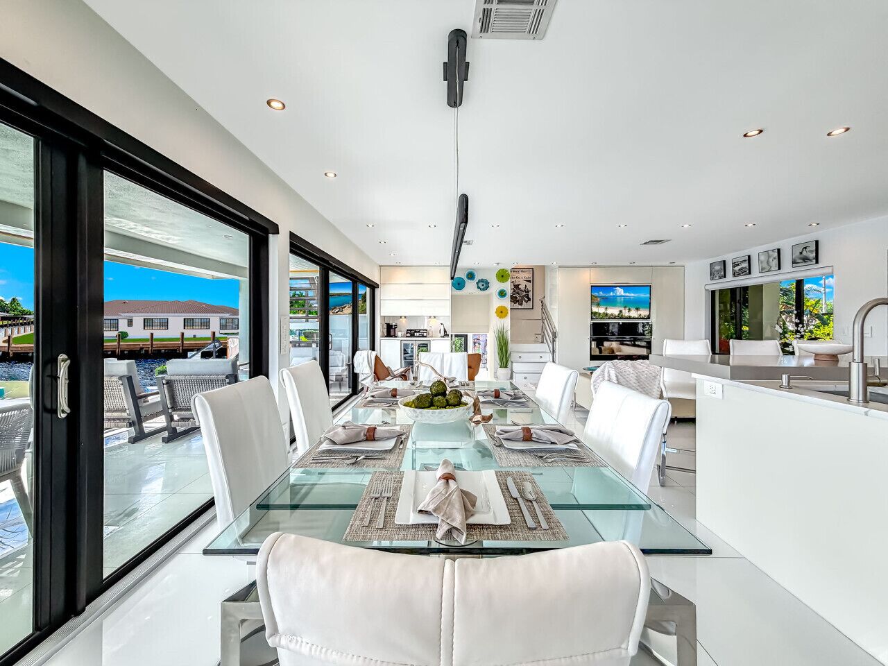 A modern dining area with a glass table, white chairs, and a view of the outdoors.