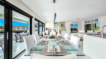 A modern dining area with a glass table, white chairs, and a view of the outdoors.