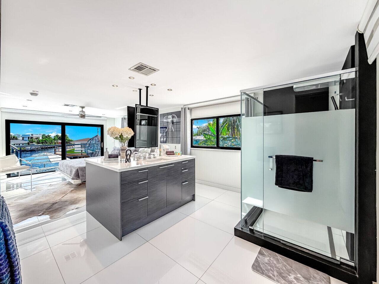A modern bathroom with a glass shower enclosure, a large mirror, and a view of a pool and cityscape.